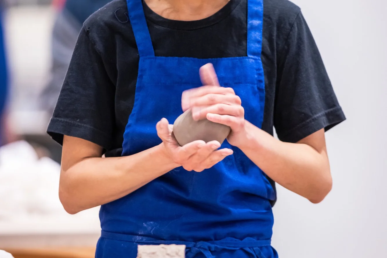 A member in a blue apron shaping clay