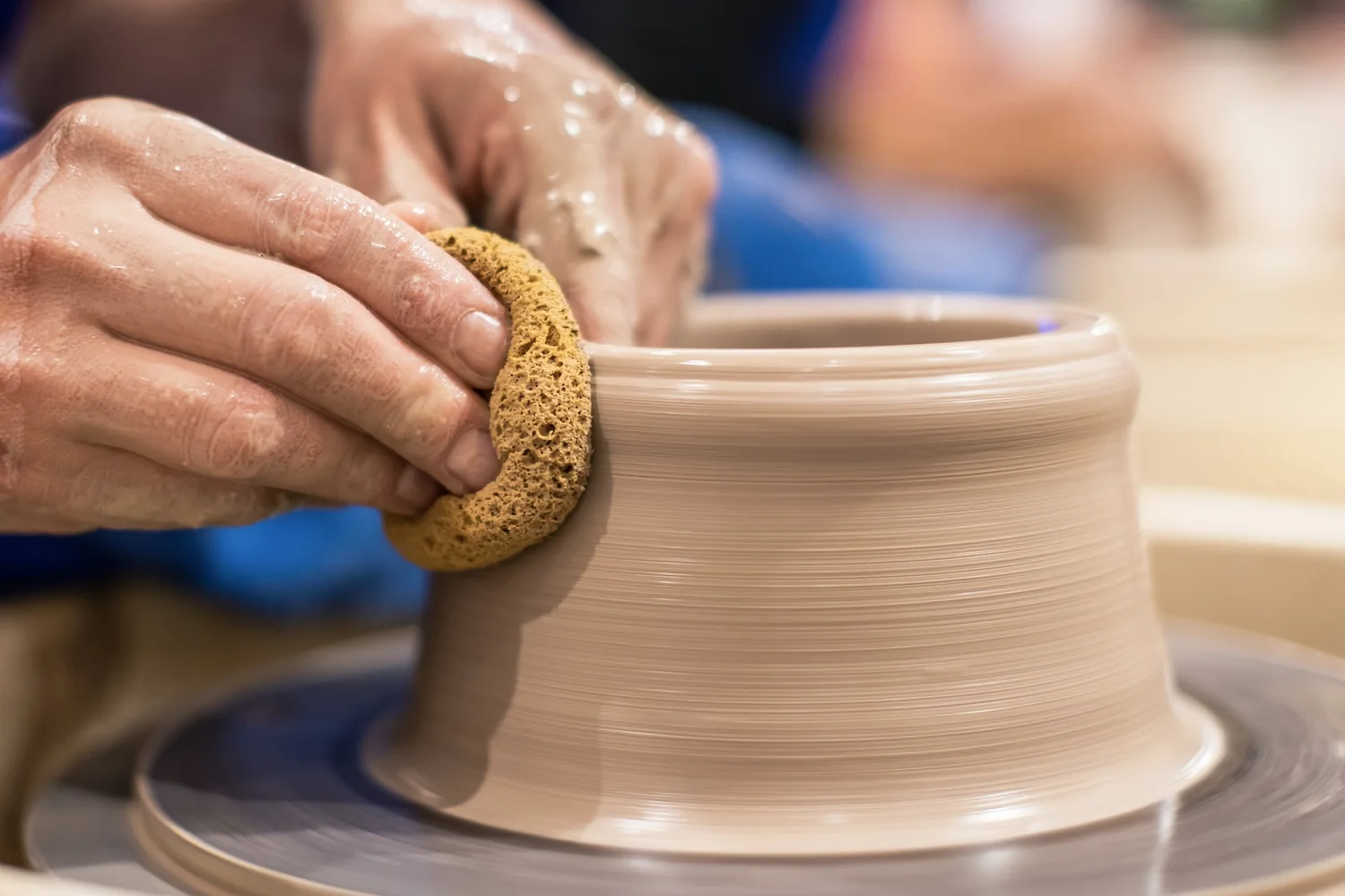 Hands smoothing a pot on the wheel with a sponge